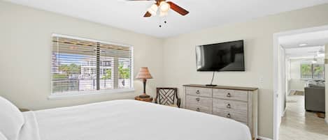 A bedroom with a bed, a ceiling fan, a TV, a window with blinds, and a dresser.