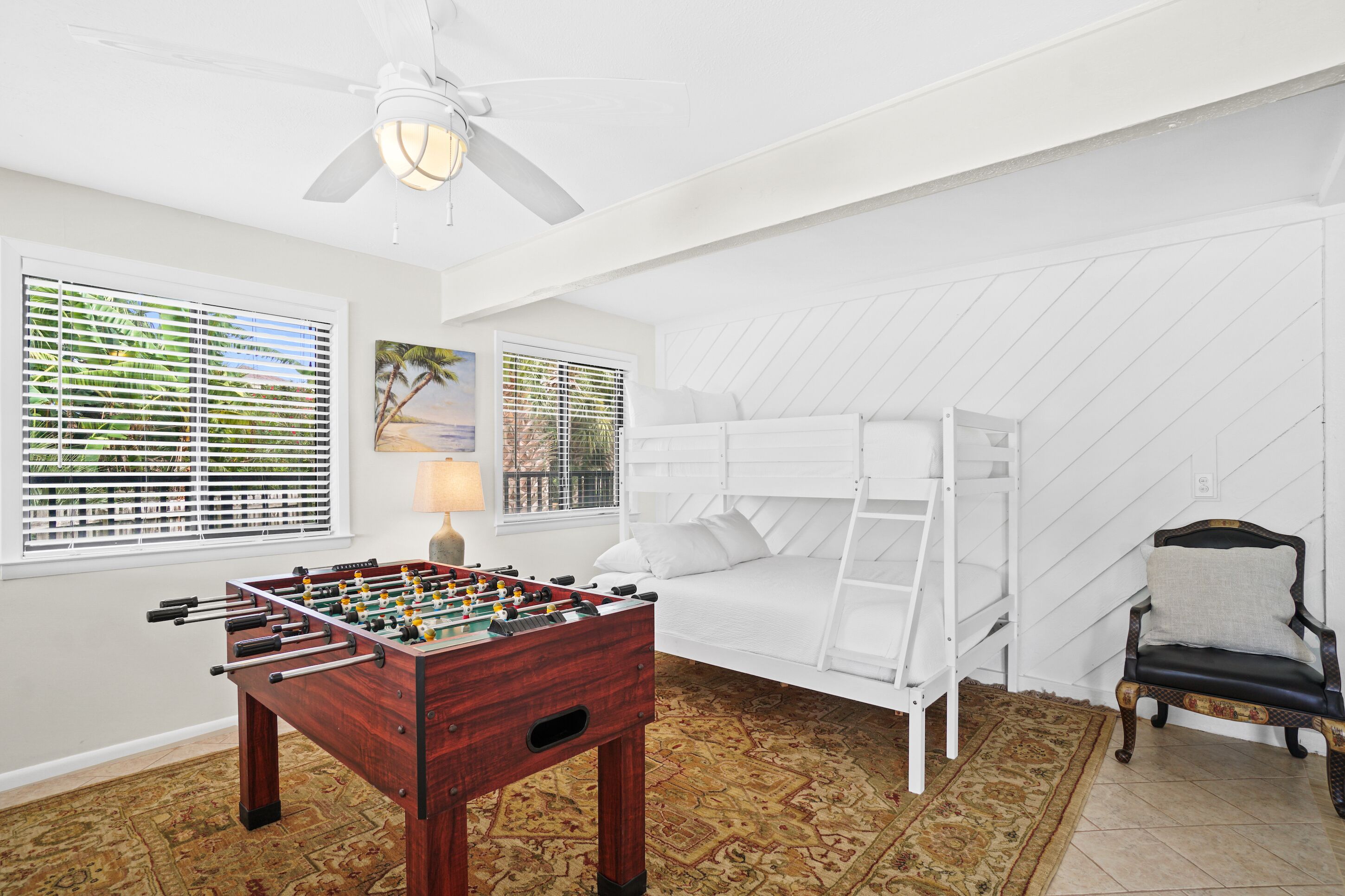 A room with a foosball table, a bed, a chair, and a ceiling fan.