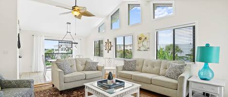 A spacious living room with a high ceiling, two sofas, a coffee table, and a ceiling fan.