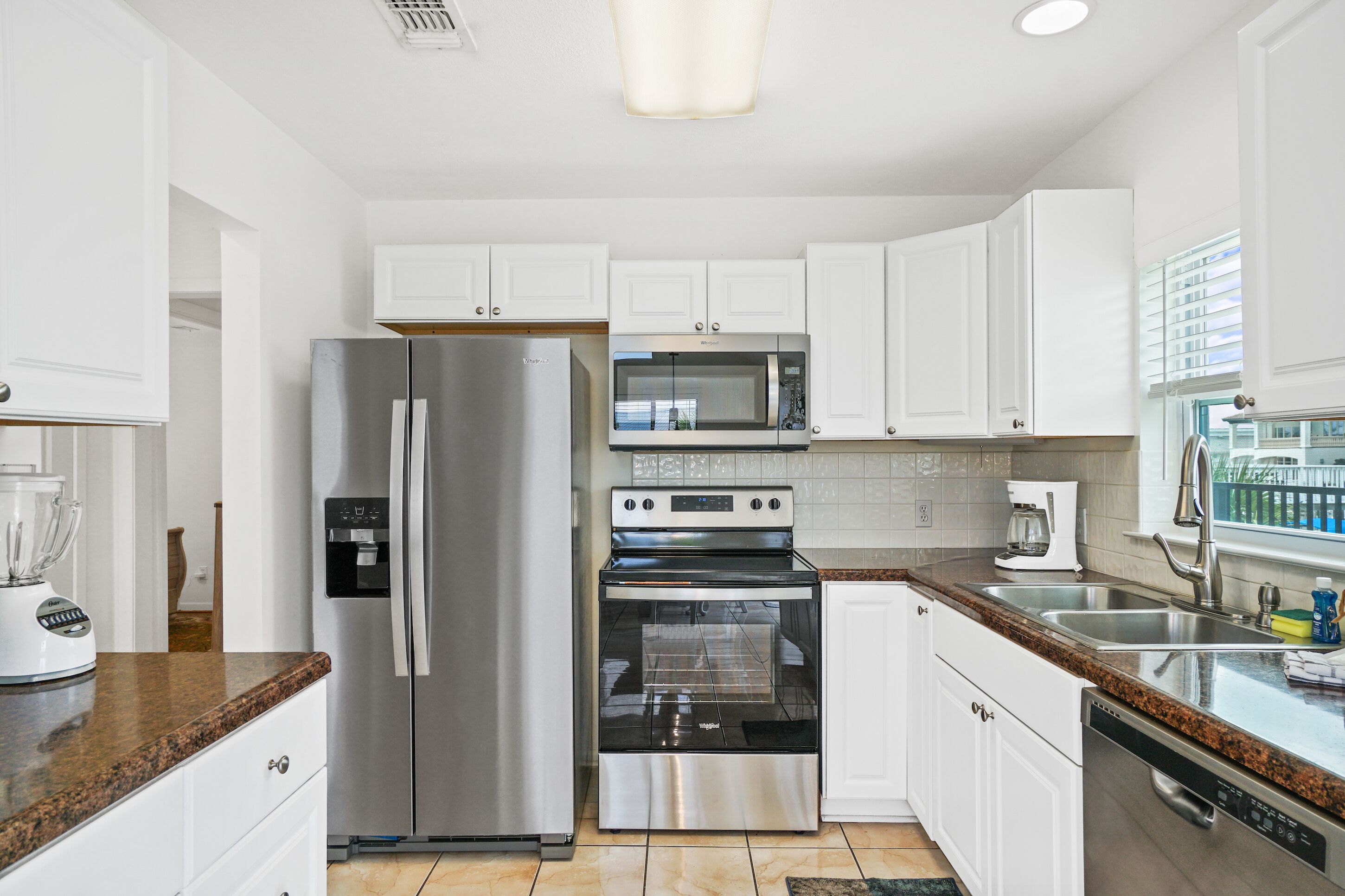 Una cocina moderna con armarios blancos, electrodomésticos de acero inoxidable, encimera de granito y una ventana con persianas.