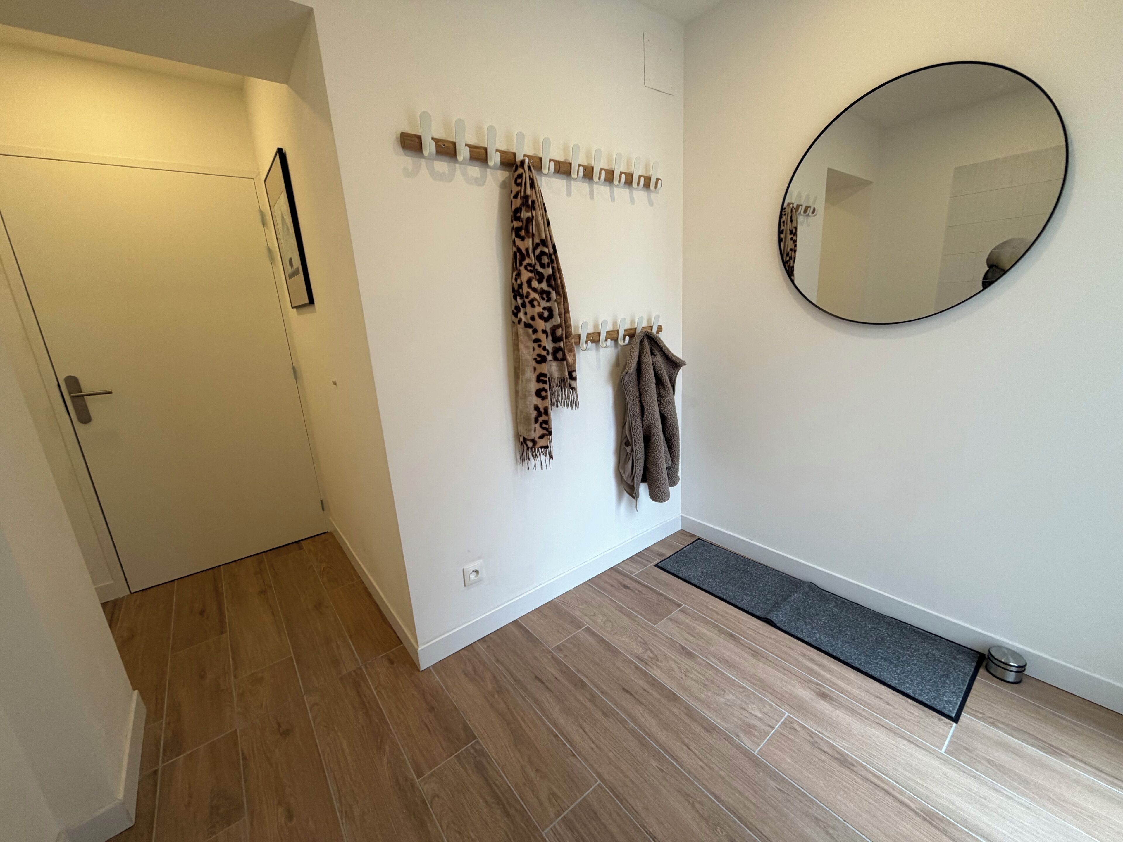 A hallway with a coat rack holding several coats, a mirror on the wall, and a door on the left.