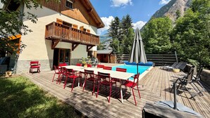 A wooden deck with a pool, red chairs, and a table. - Chalet les Ecrins - 230m2 ✨ Sauna - Swimmingpool - Garden ✨  (Vénosc, Les Deux Alpes)