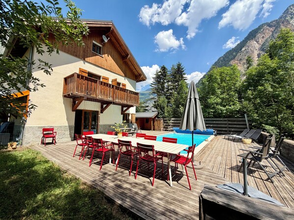 Un'area esterna con un muretto in legno, una piscina, sedie rosse e un tavolo.