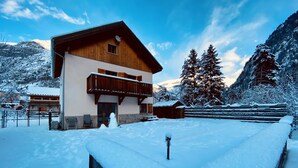 A wooden chalet with a balcony, surrounded by snow-covered mountains and trees. - Chalet les Ecrins - 230m2 ✨ Sauna - Swimmingpool - Garden ✨  (Vénosc, Les Deux Alpes)