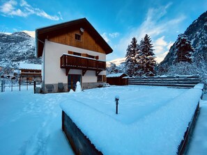 Un chalet en bois doté d’un balcon, entouré de montagnes et d’arbres couverts de neige.