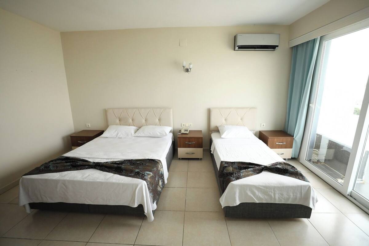 A double room with two beds, bedside tables, an air conditioning unit, and a window with curtains.