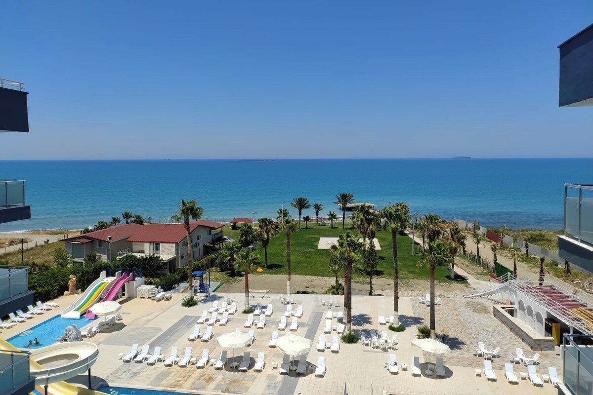 Un resort con piscina, sillas de descanso, palmeras y vista al mar.