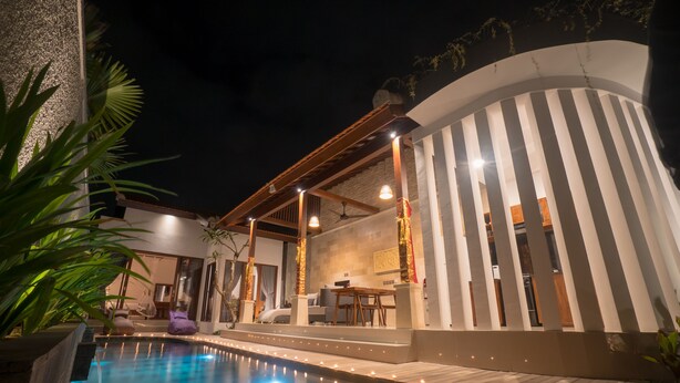 A modern pool area with a curved building, outdoor seating, and string lights. - Royani 1-Bedroom Private Pool Villa (Gianyar)