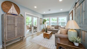 Un salón espacioso con suelo de madera, un sofá, una mesita de centro y una lámpara. Cuenta con un amplio ventanal que proporciona luz natural y vistas al exterior.