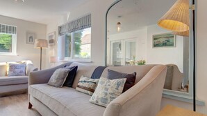 A living room with a sofa, cushions, a lamp, a mirror, and a window.