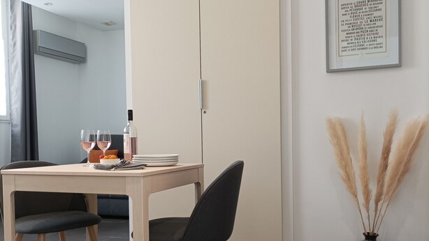 Zona pranzo moderna con tavolo in legno, due sedie, una bottiglia di vino e un testo incorniciato appeso al muro.