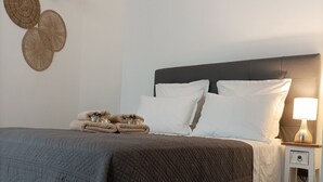 Un letto rifatto con un copriletto scuro, cuscini bianchi e un comodino con una lampada.