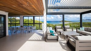 A spacious outdoor area with a wooden ceiling, large windows offering a view of the sea and greenery, and a dining area with a table and chairs. - La Siesta (4/5 Rooms) (La Baie Nettle)