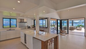 A spacious kitchen with a large island, modern appliances, and large windows offering ocean views. - La Siesta (4/5 Rooms) (La Baie Nettle)