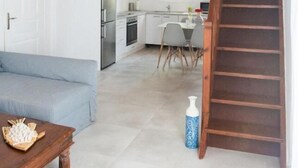 A spacious living area with a high ceiling, a wooden staircase, and a kitchen in the background. - Glamorous 2BR Villa in Ornos w Sea View (Mykonos)