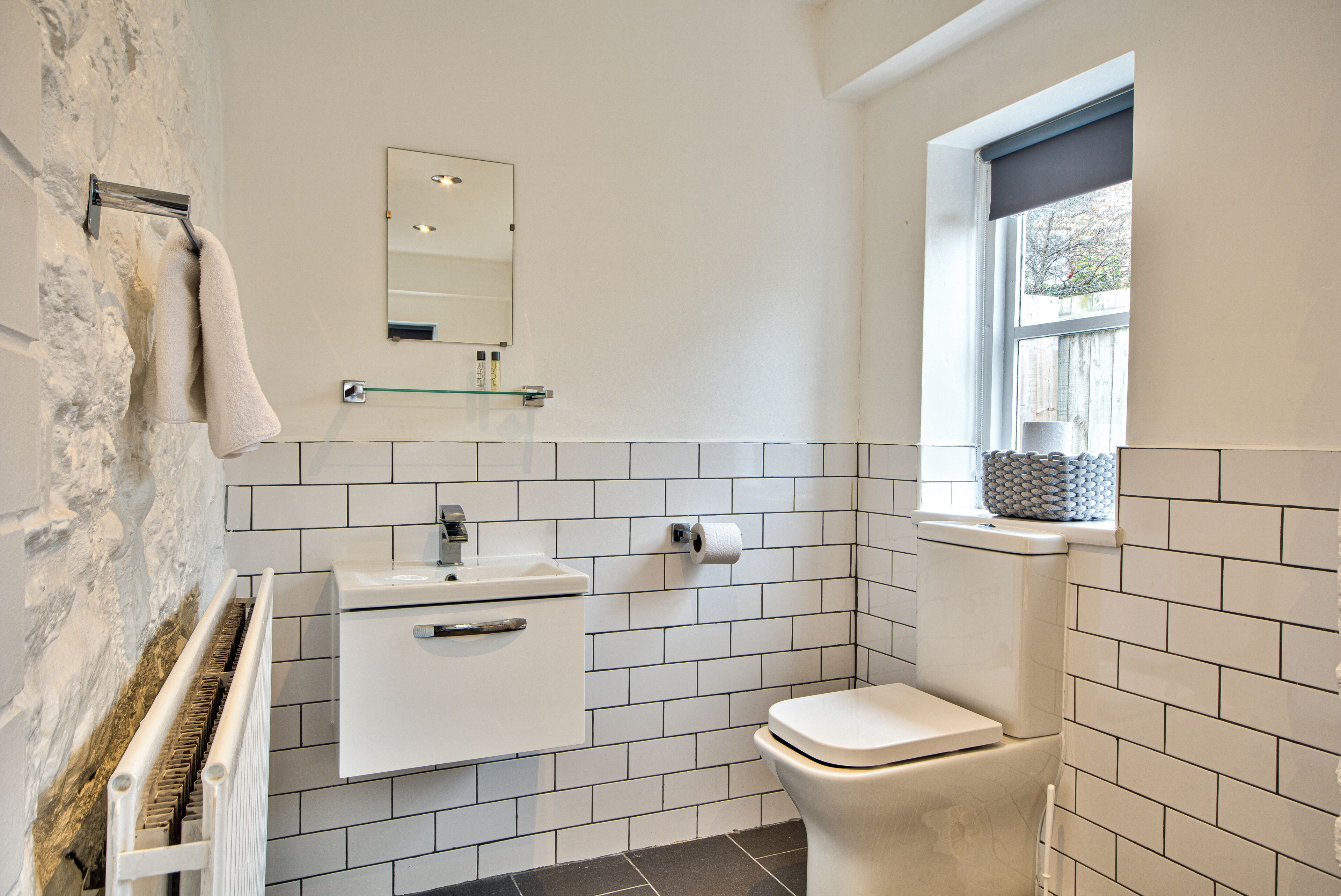 A bathroom with a white sink, a toilet, a towel rack, a mirror, and a window with a view.