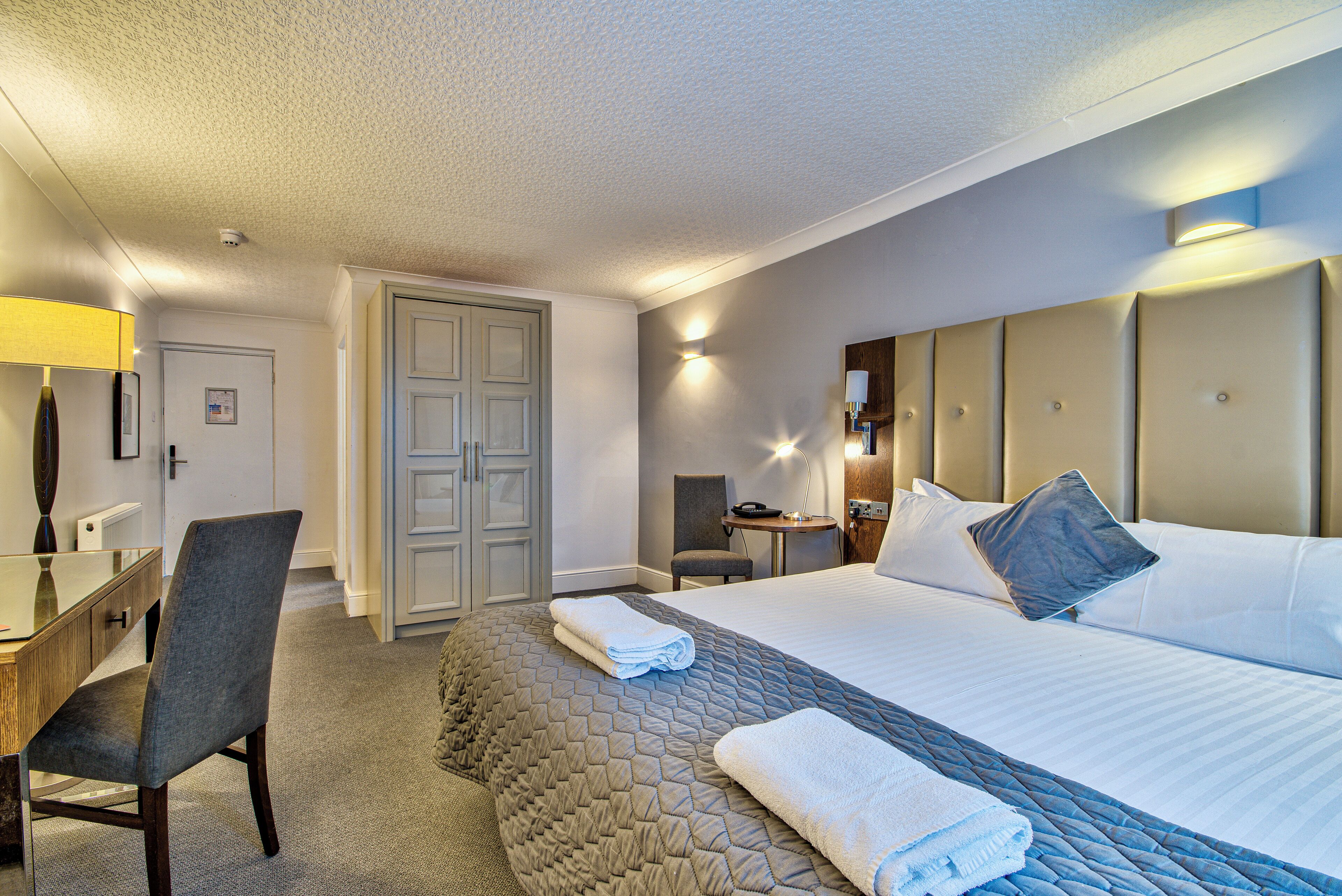 Habitación de hotel con una cama, un escritorio, una silla, una mesita y una puerta.