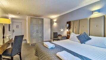 Habitación de hotel con una cama, un escritorio, una silla, una mesita y una puerta.