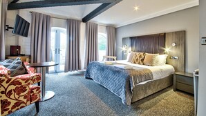 A hotel room with a bed, a chair, a small table, and a TV mounted on the wall. - The George Of Piercebridge (Darlington)
