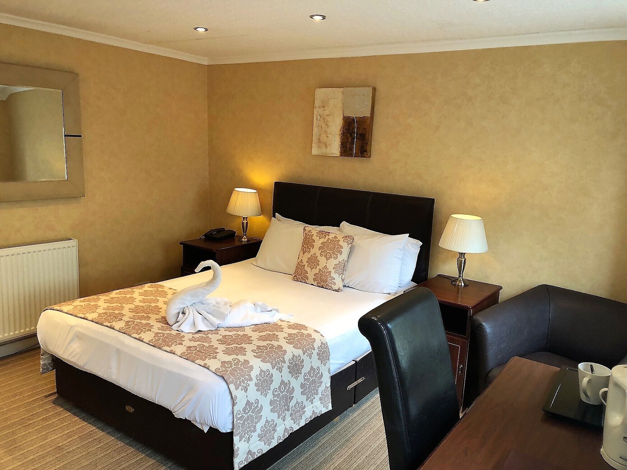 A hotel room with a bed, two bedside tables with lamps, a chair, a table with a coffee maker, and a radiator.