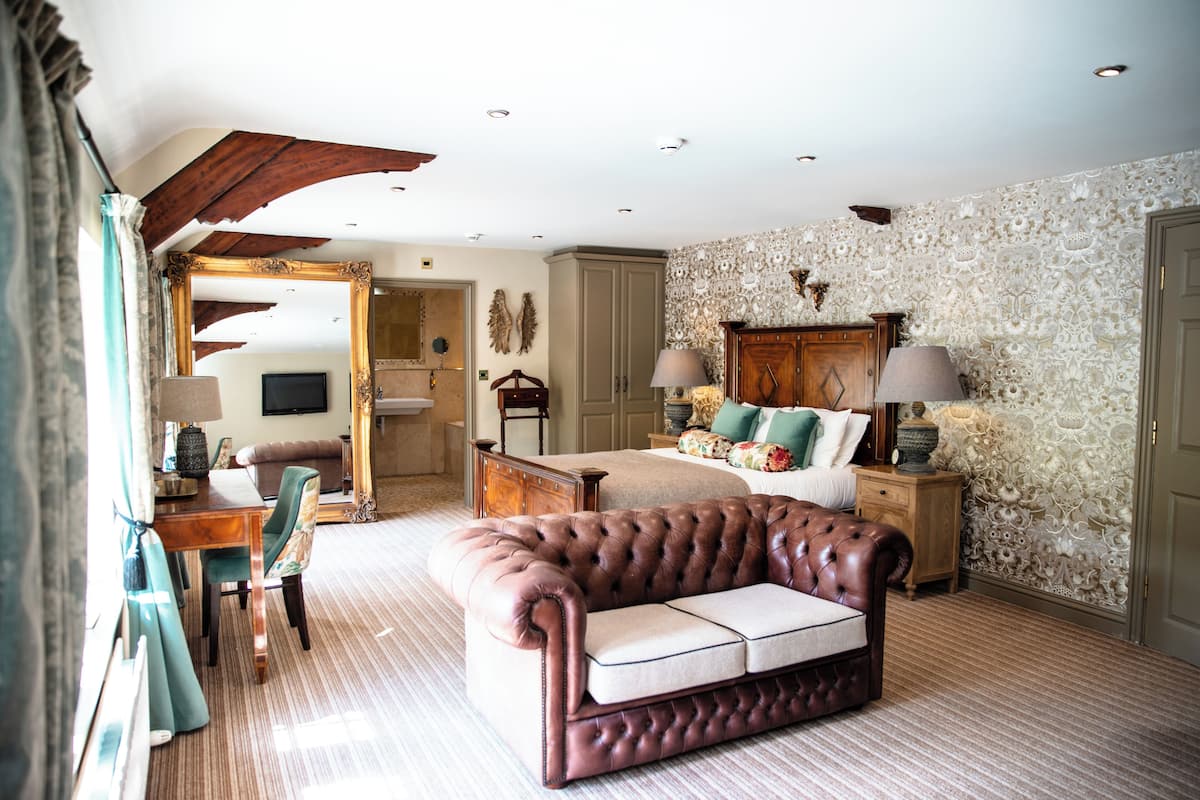 A room with a bed, a sitting area with a sofa, a wooden desk, and a chair.