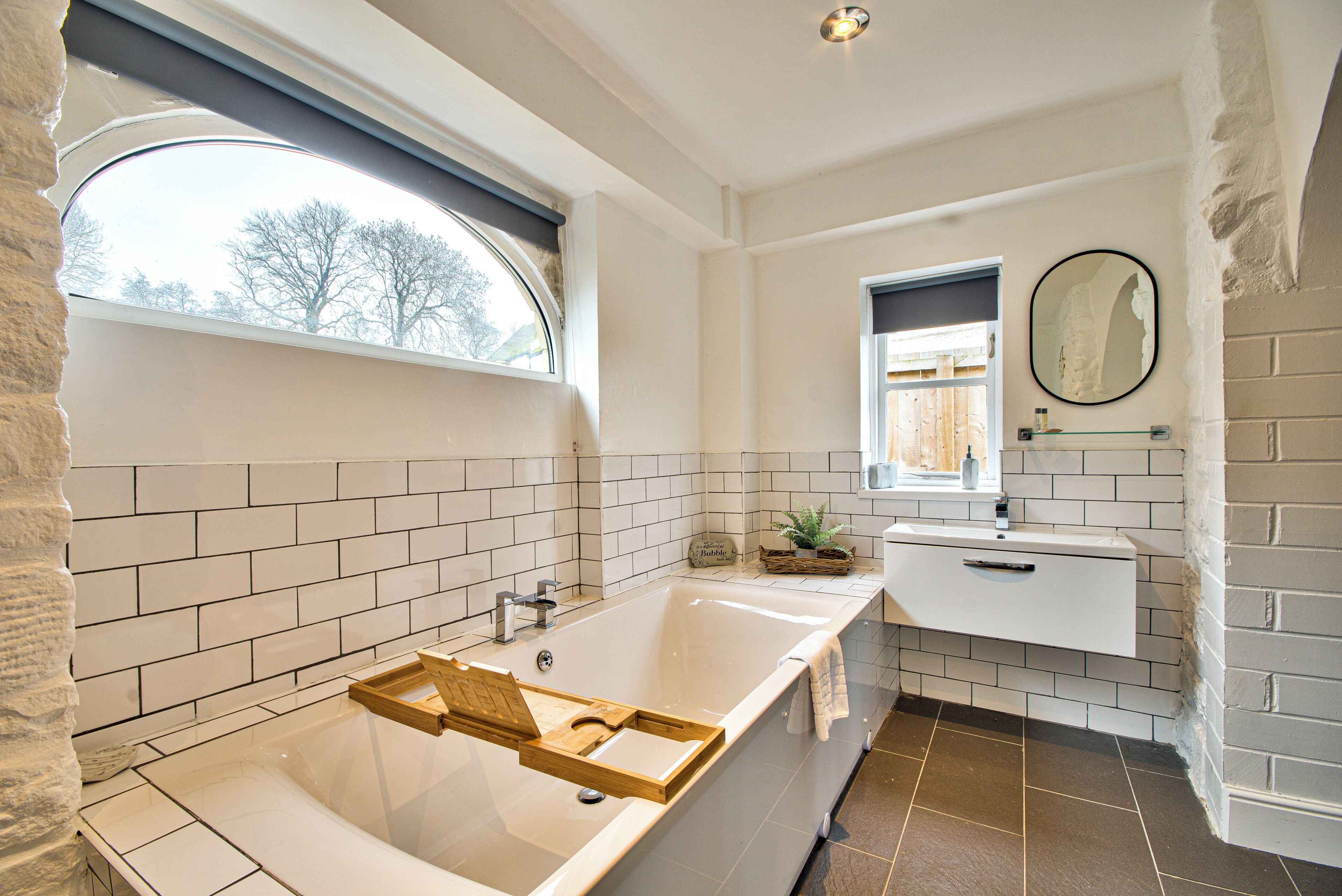 A bathroom with a bathtub, a window, a sink, and a mirror.