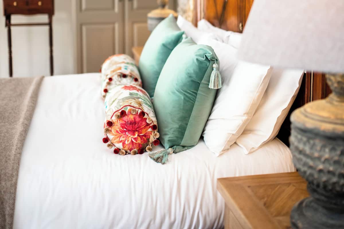 A bedroom with a bed, pillows, a nightstand, a lamp, and a wardrobe.