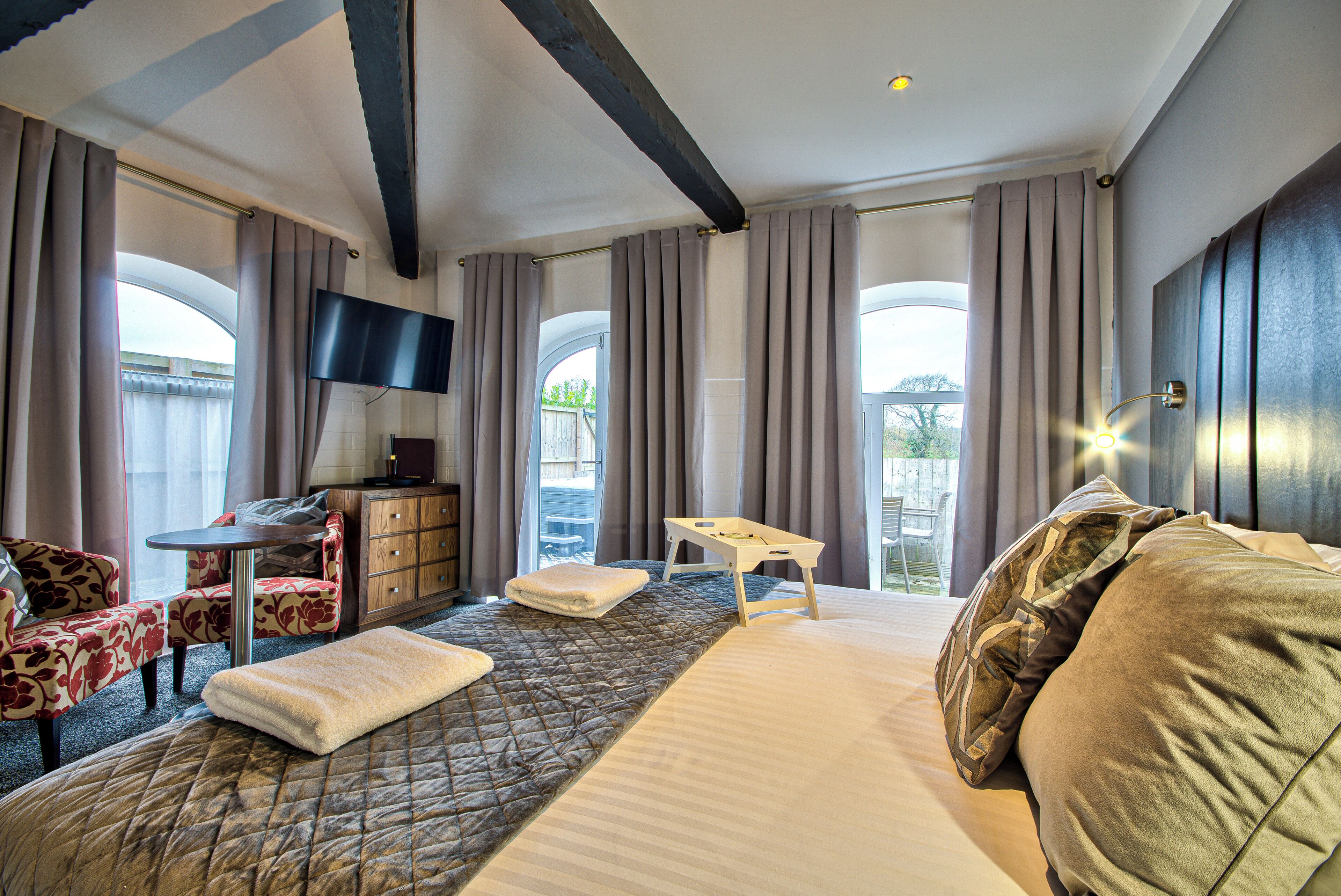 A hotel room with a bed, a desk, a chair, a TV, and large windows.
