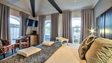 Habitación de hotel con cama, escritorio, silla, televisor y ventanas amplias.