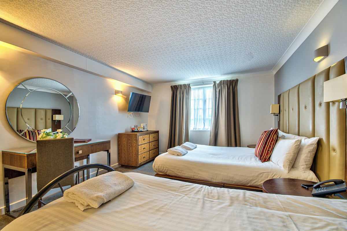 A hotel room with two beds, a desk, a chair, a dresser, a TV, and a window with curtains.
