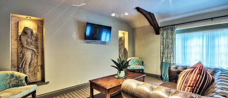 A living room with a sofa, armchair, a flat-screen TV, a statue, and a window with curtains.