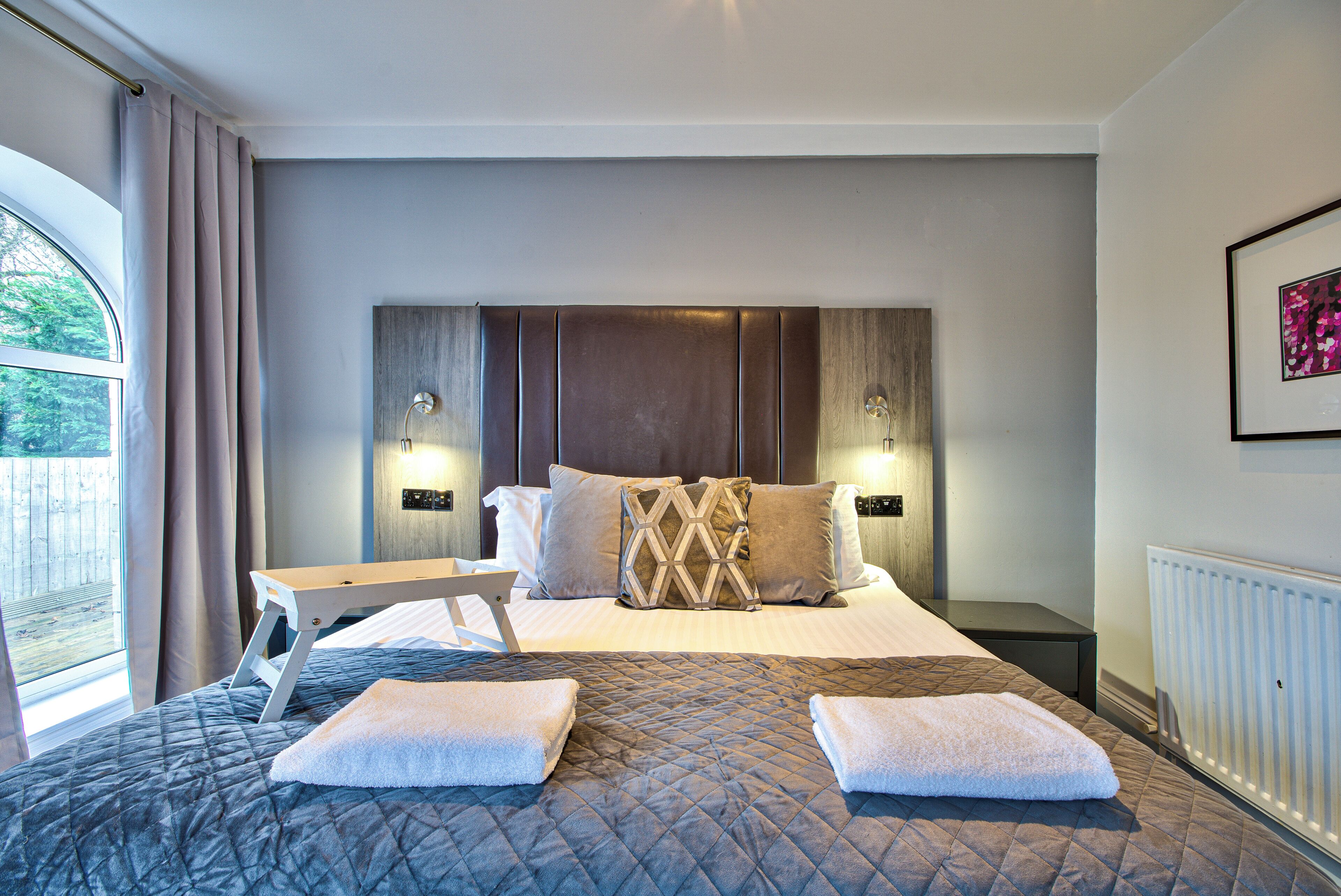 A hotel room with a large bed, bedside tables, a small desk, and a window with curtains.