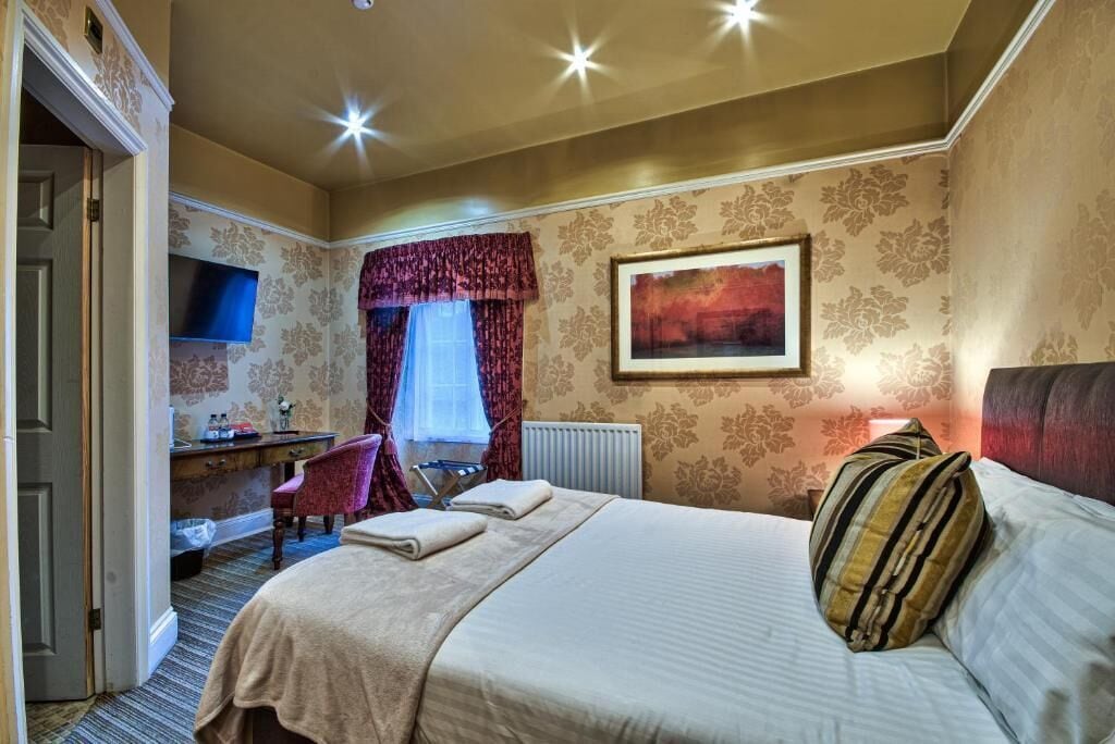 A hotel room with a bed, a desk, a chair, a television, and a painting on the wall.