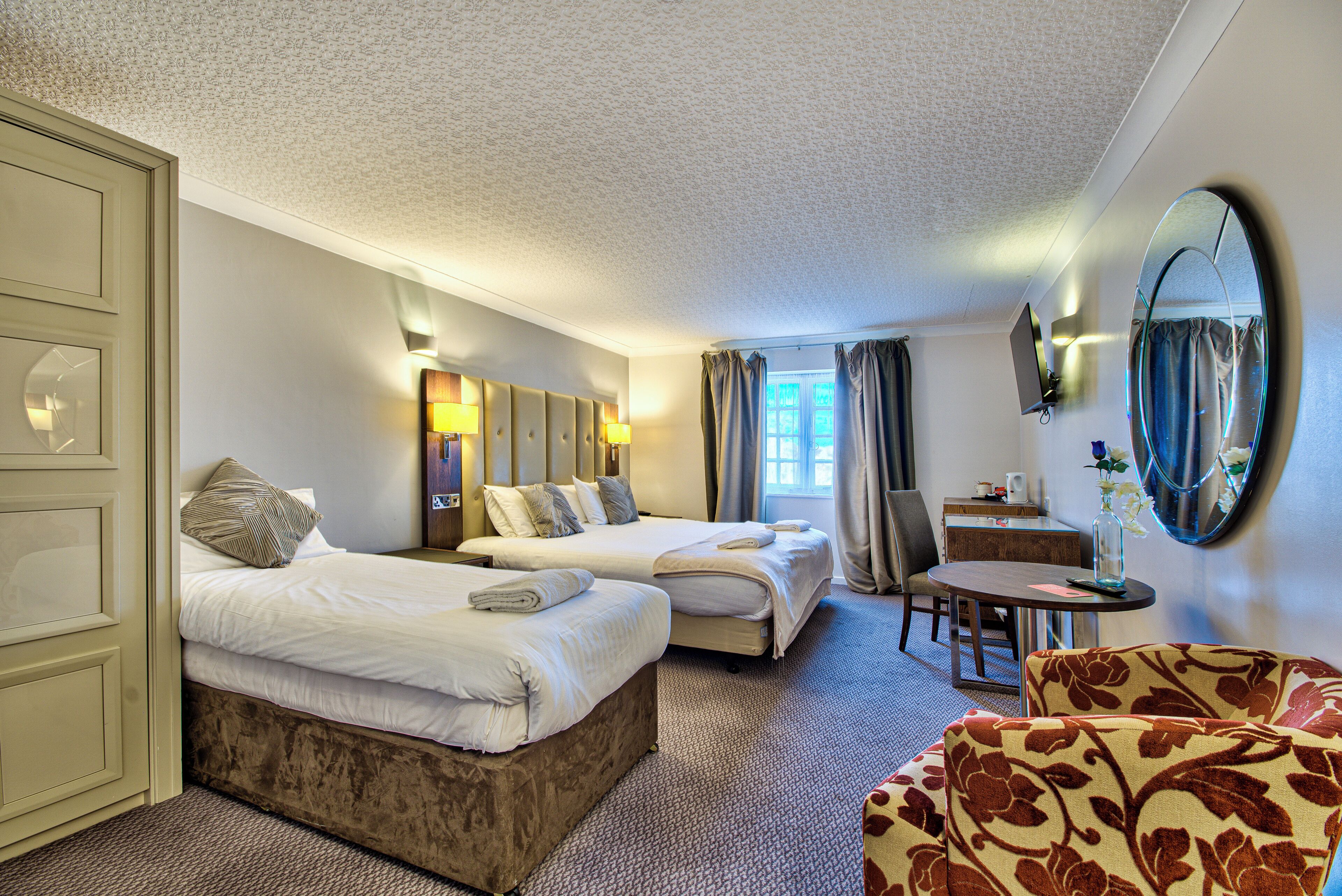 A hotel room with two beds, a desk, a chair, and a large mirror.