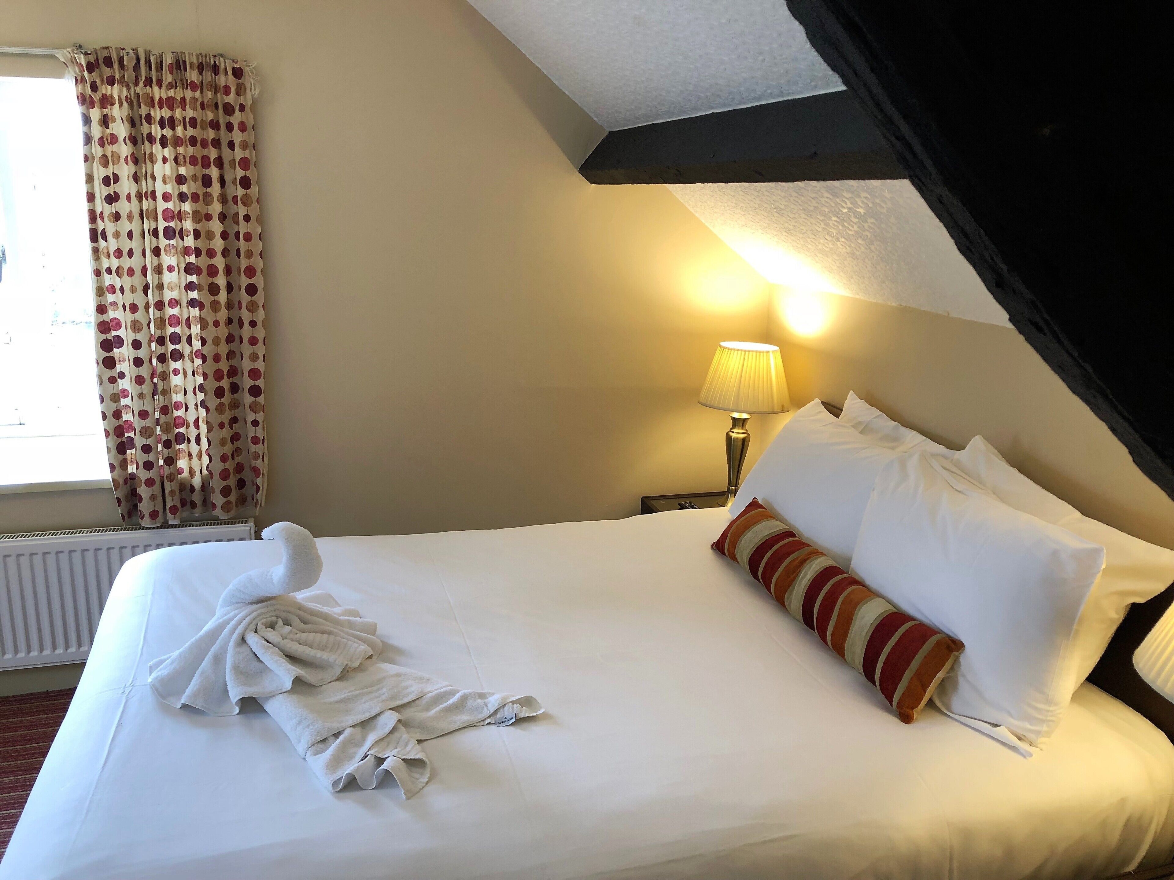 A neatly made bed with white linens, a striped pillow, and a white towel.