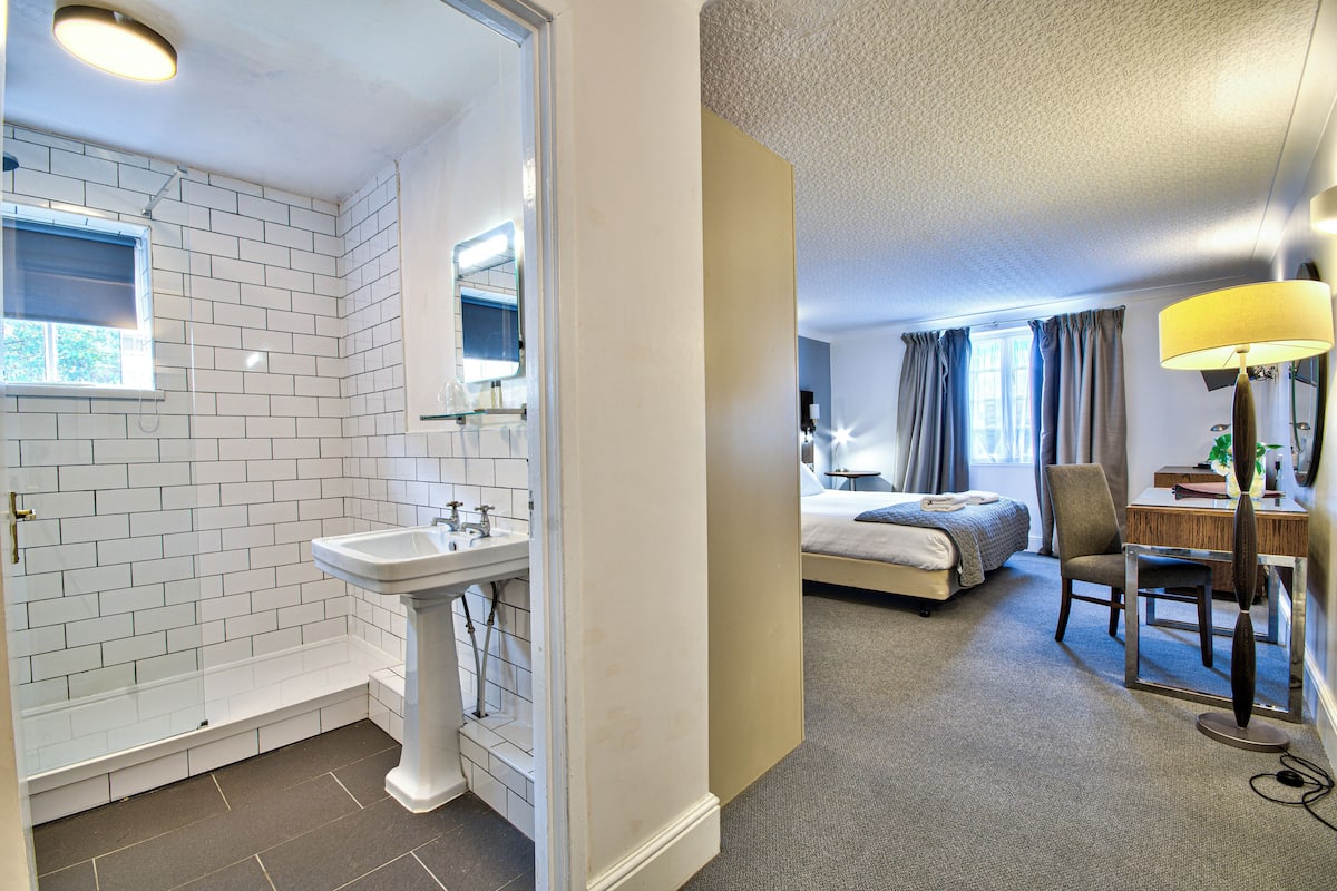 A hotel room with a bathroom, a bed, a desk, and a chair.
