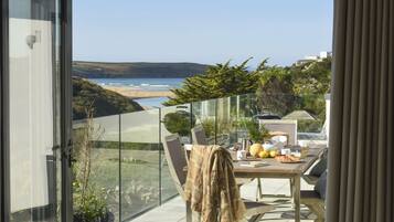 A balcony with a table set for breakfast, overlooking a beach and hills.