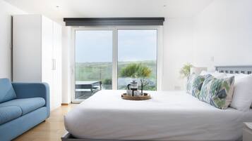 A bedroom with a large bed, a blue sofa, a coffee table with a tray, and a view of greenery through a sliding door.