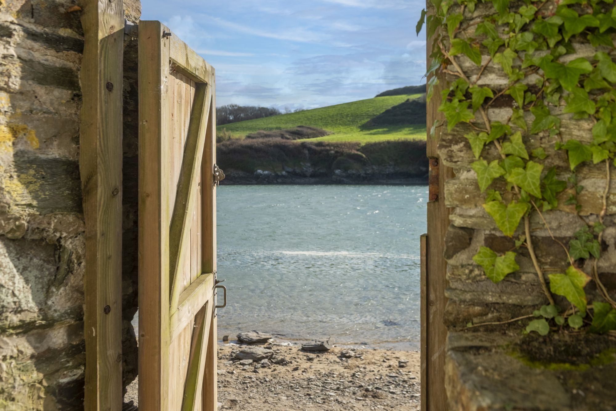 A wooden gate leading to a beach with a stone wall and greenery on one side.