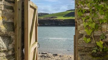 A wooden gate leading to a beach with a stone wall and greenery on one side.