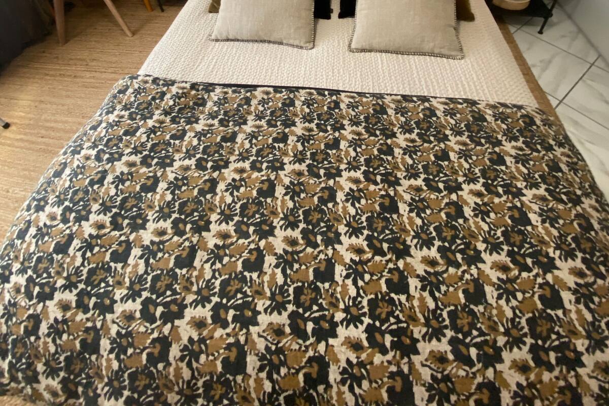 Un dormitorio con cabecera capitonada, cama con dos almohadas, colcha estampada, escritorio con silla y dos lámparas de noche.