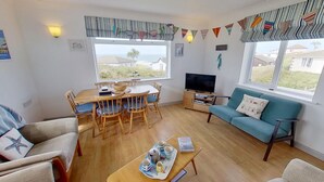 A living room with a wooden dining table, blue sofa, and a TV. - C41 Windmills, Riviere Towans (Hayle)