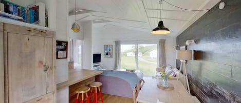 A cozy room with a wooden dining table, red bar stools, a TV, and a large window offering a view of the outdoors.