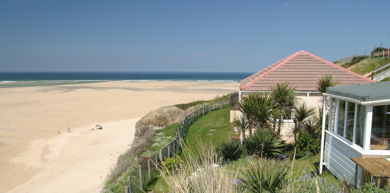 Una propiedad frente a la playa con una casa, una playa de arena y un cielo despejado.