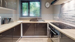 A modern kitchen with a built-in oven, a sink, and a window with blinds. - 48 Trevithick Court, Tolroy Manor (Hayle)