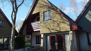 Stylish two-story home with a gabled roof and balcony, featuring a large sliding glass door entrance and outdoor seating area.