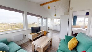 Un salon moderne avec un téléviseur, un canapé et une table basse. Il y a également un coin cuisine avec des placards et une fenêtre.