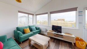 Un salon chaleureux avec un canapé vert, une table basse en bois et un téléviseur posé sur un meuble blanc.