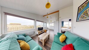 Un vaste espace de vie doté de grandes fenêtres, d’une table basse en bois et de canapés de couleur turquoise.