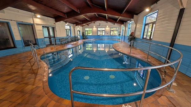 Une piscine intérieure avec un sol carrelé, des rampes en métal et un plafond en bois.